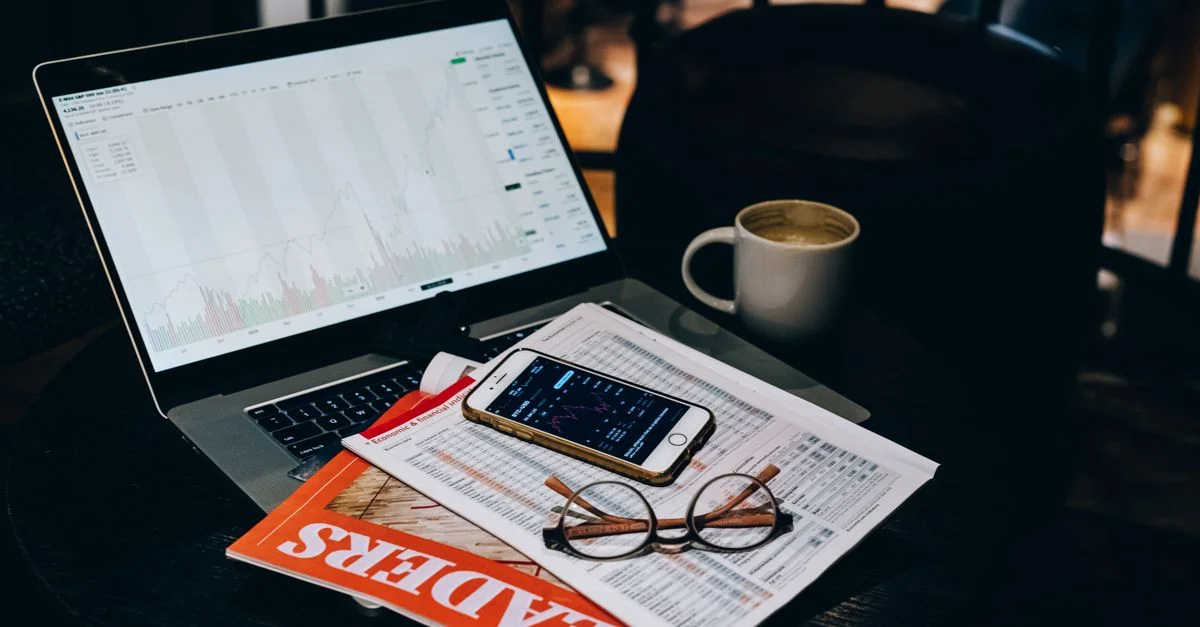 Un aménagement de bureau confortable avec un ordinateur portable affichant des graphiques boursiers, du café et des documents.