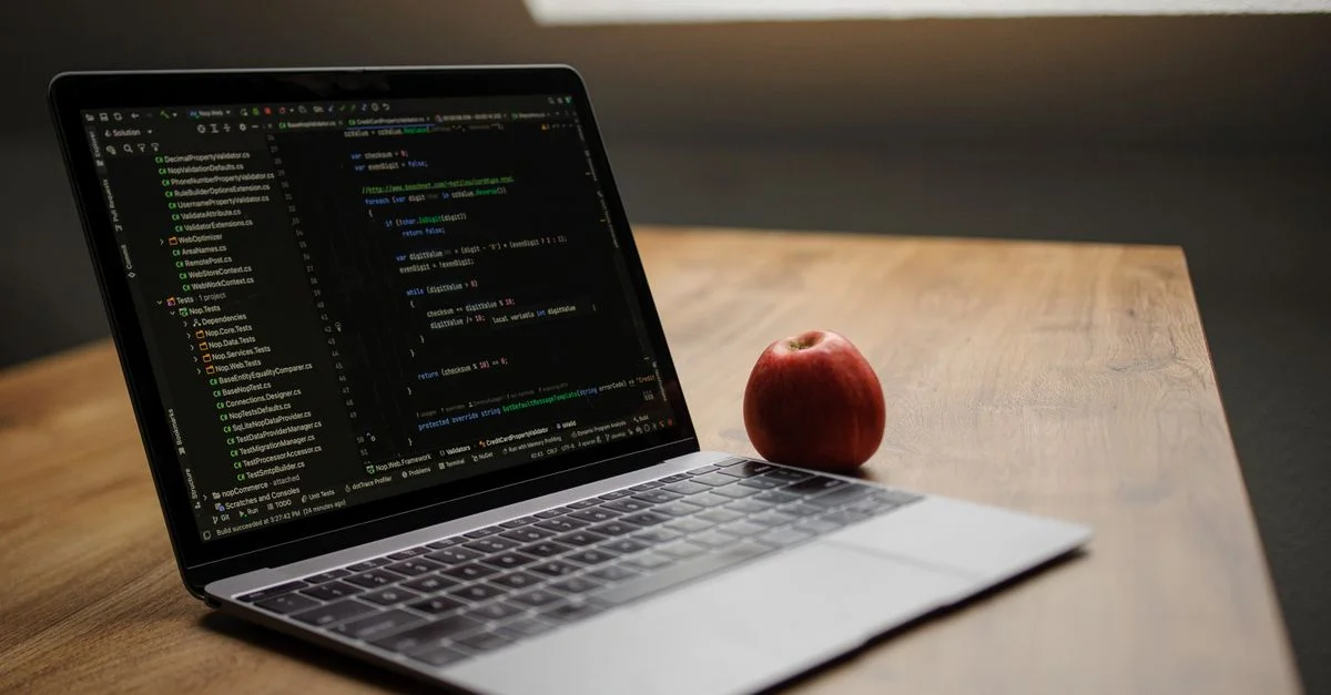 Ordinateur portable ouvert affichant du code à côté d'une pomme rouge sur un bureau en bois.